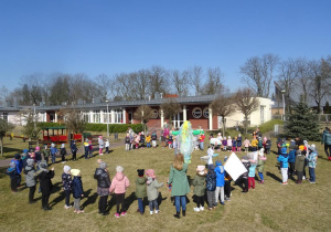 Dzieci stoją w kole w ogrodzie przedszkolnym wokół kukły Marzanny, biją brawa.